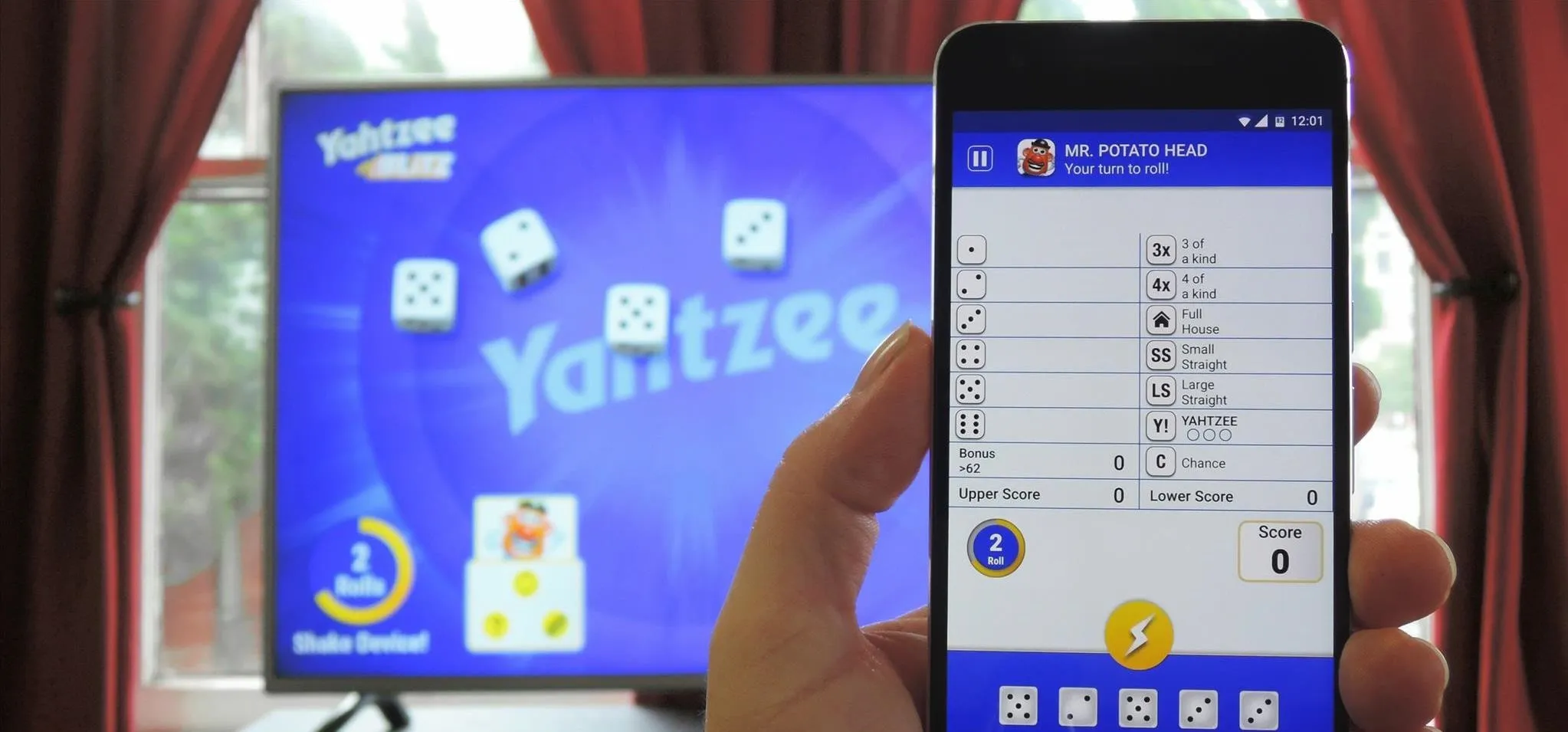 Person playing Yahtzee on a smartphone while the game is displayed on a TV screen.