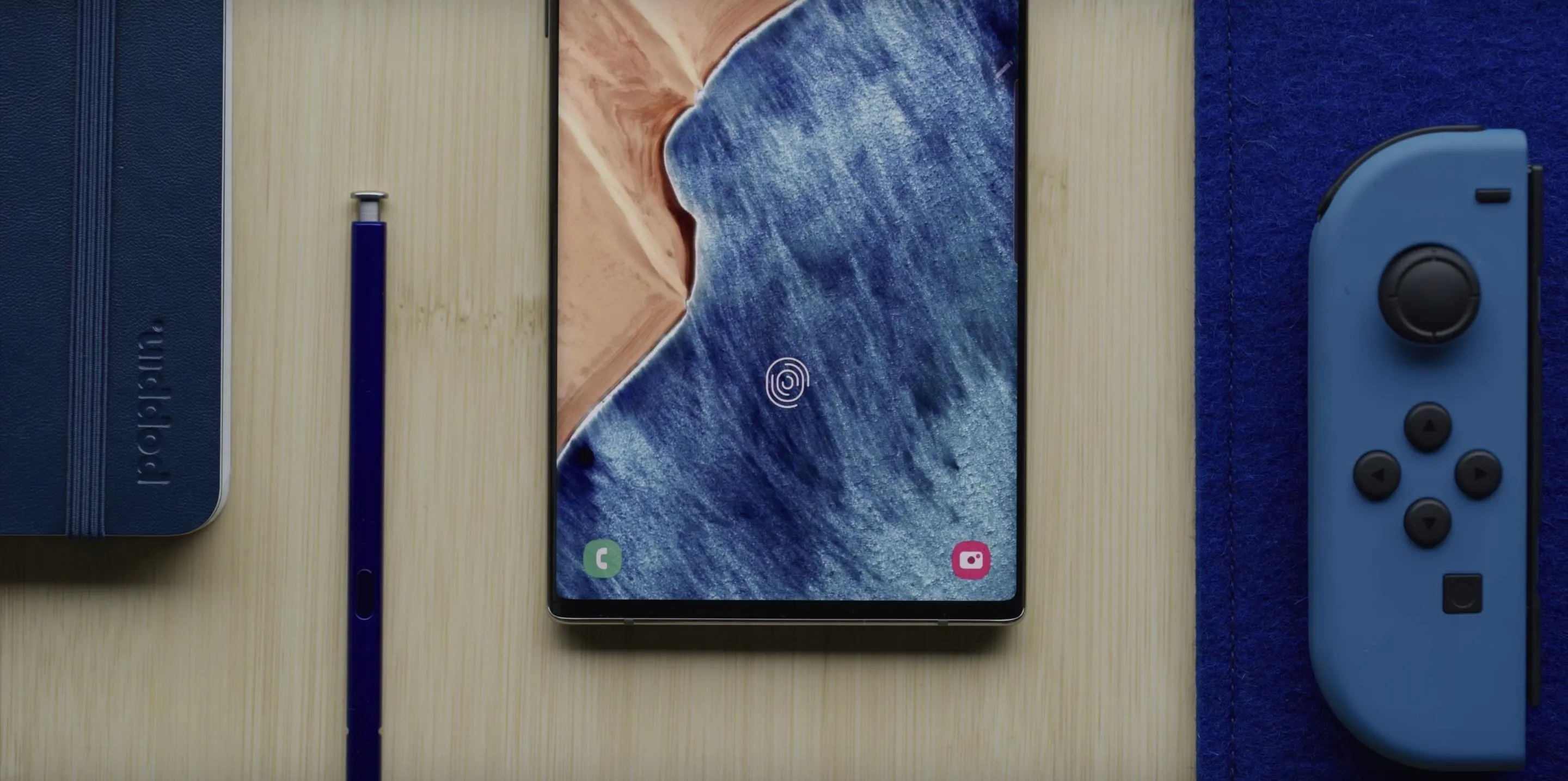 A smartphone placed on a wooden surface alongside a stylus and a gaming controller.